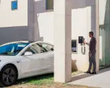 Uomo accanto a un'auto elettrica bianca, che interagisce con una wallbox V2C. Un bonus per la ricarica intelligente.