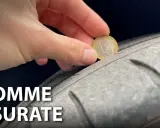 Una mano inserisce una moneta da 1 euro in un solco di uno pneumatico per mostrare come vedere se le gomme sono consumate.