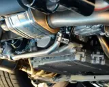 Dettaglio del sistema di scarico di un'auto, con il tubo di scappamento auto lucido e altri componenti metallici.