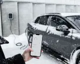 Persona controlla la carica di auto elettriche con lo smartphone, mentre nevica. Il freddo non ferma la tecnologia.
