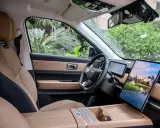 Interni del Jaecoo 7: sedili in pelle beige e nera, volante moderno e un grande schermo centrale con paesaggio montano.