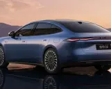 BYD Seal 08, berlina blu elettrica, riflette sull'acqua al tramonto, con montagne sullo sfondo.