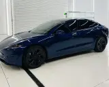Una splendida Tesla piccola, blu scuro, con cerchi neri lucidi, parcheggiata in un garage pulito e illuminato.