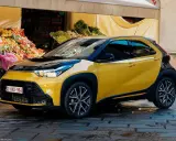 Toyota Aygo X gialla parcheggiata davanti a un mercato. Nessun problema visibile, solo un'auto elegante.