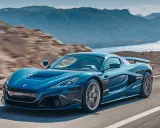 La Rimac Nevera blu sfreccia su una strada panoramica, con montagne e acqua sullo sfondo.