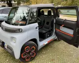 Un'auto elettrica due posti grigia con dettagli arancioni, porte aperte, sedili neri e cerchi distintivi.