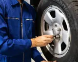 Meccanico in tuta blu controlla i bulloni di una ruota. Ci si chiede dopo quanti km si cambiano le gomme per sicurezza.