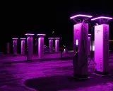 Stazione di ricarica Ionity Italia di notte, illuminata da luci viola. Colonne moderne con logo e cavi pronti per le auto elettriche.