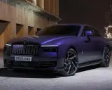 Una Rolls-Royce sportiva viola metallizzato, con un design audace e cerchi neri, parcheggiata di notte vicino a un porto industriale.
