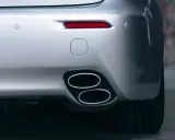 Doppio scarico cromato su un'auto sportiva argentata, parte del collettore di scarico. Sensori di parcheggio e fanale posteriore rosso visibili.