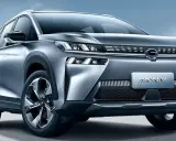 Un SUV grigio metallizzato, l'Aion V, con un design moderno e fari a LED affilati, si presenta su uno sfondo blu cielo.