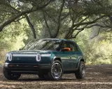 Un'avventura elettrica ti aspetta con la **Rivian R3X** verde bosco, pronta ad affrontare sentieri tra gli alberi.