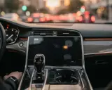 Interno di un'auto moderna, con cambio automatico e schermo touch. La mano del guidatore è sul cambio, pronto per un viaggio in **auto hold golf**.