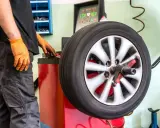 Meccanico con guanti arancioni effettua bilanciatura ruota. Scopri il costo inversione gomme per la tua sicurezza.