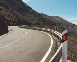 Strada tortuosa in montagna con guardrail e segnali di pericolo. I catadiottri cosa sono? Sono quei dispositivi che riflettono la luce per segnalare la strada.