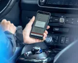 Mano che tiene uno smartphone con app di navigazione attiva, mostrando il **power cruise control** per un viaggio in auto.