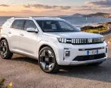 Un'imponente Fiat, quasi un giga panda, sfreccia su una strada costiera al tramonto.