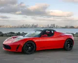 Tesla Roadster rosso fiammante, con la silhouette di una città all'orizzonte.