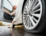 Donna esce dall'auto con gomme sgonfie sul bagnato.