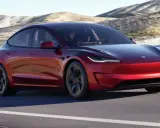 Tesla Model 3 rossa su strada panoramica. Il suo peso è ottimizzato per prestazioni elettriche.