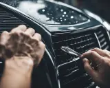 Mani che lavorano per togliere graffi auto profondi fai da te, lucidando la griglia con cura.