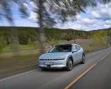 La Hyundai Ioniq 5 sfreccia su una strada panoramica tra alberi e colline verdi, con un cielo nuvoloso.
