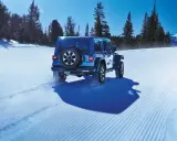Un blu Jeep Wrangler affronta la neve con pneumatici Toyo Open Country AT3, lasciando tracce su un sentiero battuto tra alberi innevati e montagne.