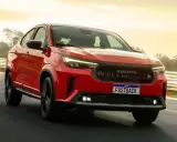 La Fiat Fastback 2026 rossa sfreccia su una pista, con il sole che illumina il cielo.
