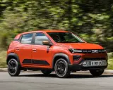 Dacia Spring arancione in movimento, la sua compatta lunghezza la rende ideale per la città.