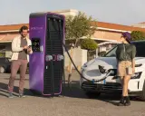 Coppia in una stazione di ricarica Enel X Way. Lei attende mentre l'auto si carica, lui controlla lo smartphone. Ottime recensioni per questa stazione di ricarica.