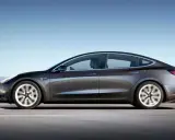 Tesla grigia in movimento su strada, con un conducente al volante. Quanti km fa una Tesla? Dipende dal modello e dalla batteria.