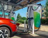 Un'auto rossa si ricarica presso colonnine ultra fast sotto pannelli solari.