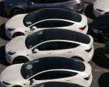 Parcheggio di auto elettriche in Italia, con modelli bianchi e grigi in fila, pronti per la consegna.