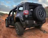 Un fuoristrada elettrico Jeep nero affronta un sentiero sterrato nel deserto, con le portiere aperte e una ruota di scorta sul retro.