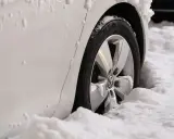 Ruota di un'auto bianca sommersa dalla neve. Il freno a mano ghiacciato rende difficile muoversi.