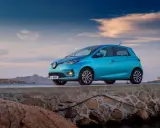 Un'elegante Renault Zoe blu, uno dei tanti modelli Renault, è parcheggiata su un muretto di pietra con il mare e le montagne sullo sfondo.
