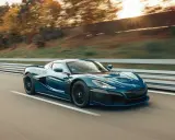 La **auto elettrica più veloce** sfreccia su una strada, con il sole che tramonta tra gli alberi sullo sfondo.