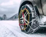 Catene da neve senza codice: come riconoscerle. Ruota di un'auto con catene montate su strada innevata.
