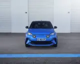 La nuova Alpine A290, un'auto elettrica sportiva blu brillante, attende il suo momento davanti a un garage con porte chiuse.