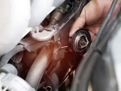 Mano che rimuove il termostato macchina, componente essenziale per il controllo della temperatura del motore.