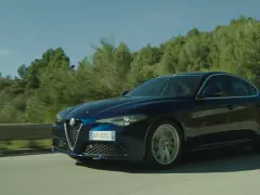Alfa Romeo blu sfreccia su strada panoramica. Il **significato** di "JTDm" è legato ai motori diesel Alfa Romeo.