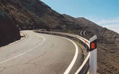 Strada tortuosa in montagna con guardrail e segnali di pericolo. I catadiottri cosa sono? Sono quei dispositivi che riflettono la luce per segnalare la strada.