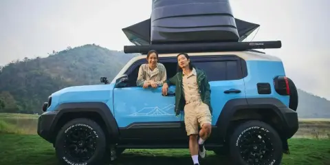 Coppia sorridente accanto a un toyota land cruiser mini blu, pronto per l'avventura con tettoia e box sul tetto.