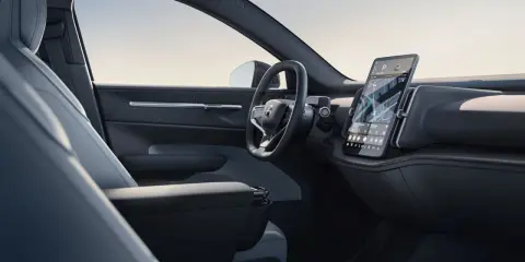 Interni minimalisti del Volvo EX30: sedili chiari, volante moderno e grande schermo centrale con navigazione.