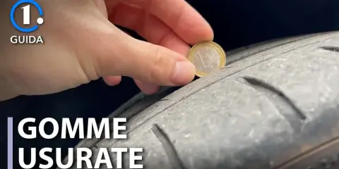 Una mano inserisce una moneta da 1 euro in un solco di uno pneumatico per mostrare come vedere se le gomme sono consumate.