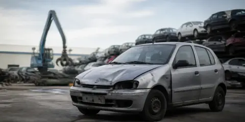 Un'auto argento, probabilmente destinata alla rottamazione Euro 5, in un deposito di veicoli con un escavatore in sottofondo.
