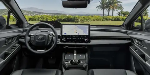 Interni moderni della Toyota bz4x con ampio display centrale e volante multifunzione. Navigazione attiva per un viaggio panoramico.
