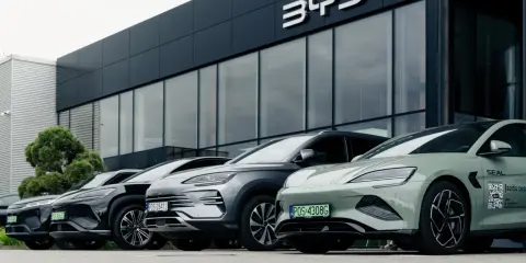Vari modelli di auto BYD parcheggiati davanti a uno showroom moderno.