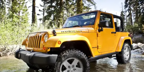 Jeep Wrangler 2.8 CRD in giallo, immerso in un ruscello tra alberi. Un'avventura che potrebbe presentare qualche problema.