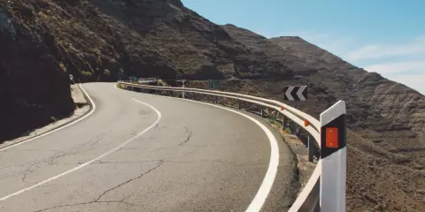 Strada tortuosa in montagna con guardrail e segnali di pericolo. I catadiottri cosa sono? Sono quei dispositivi che riflettono la luce per segnalare la strada.